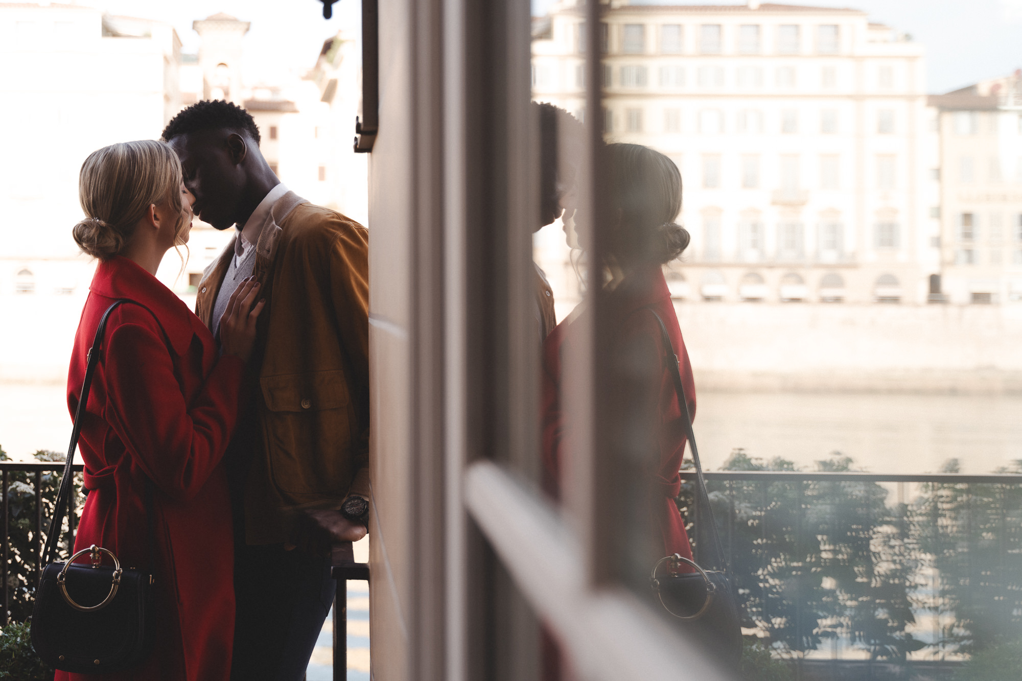Intimate couple portrait reflected in a glass window overlooking the Arno river in Florence.