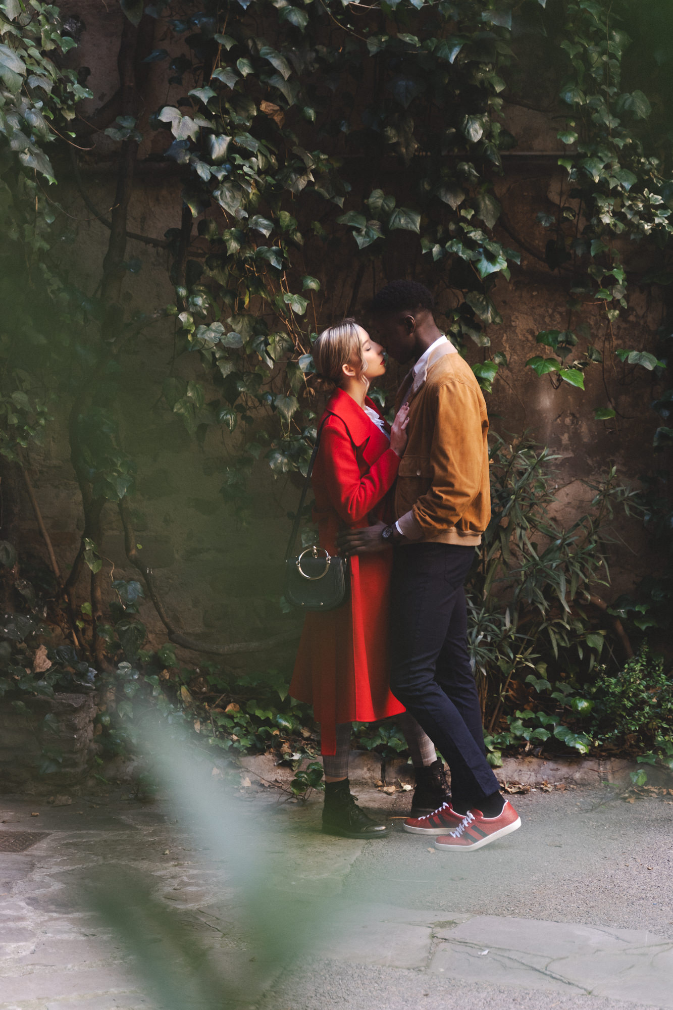 Couple embracing in front of a wall covered in green and brown autumn vines.