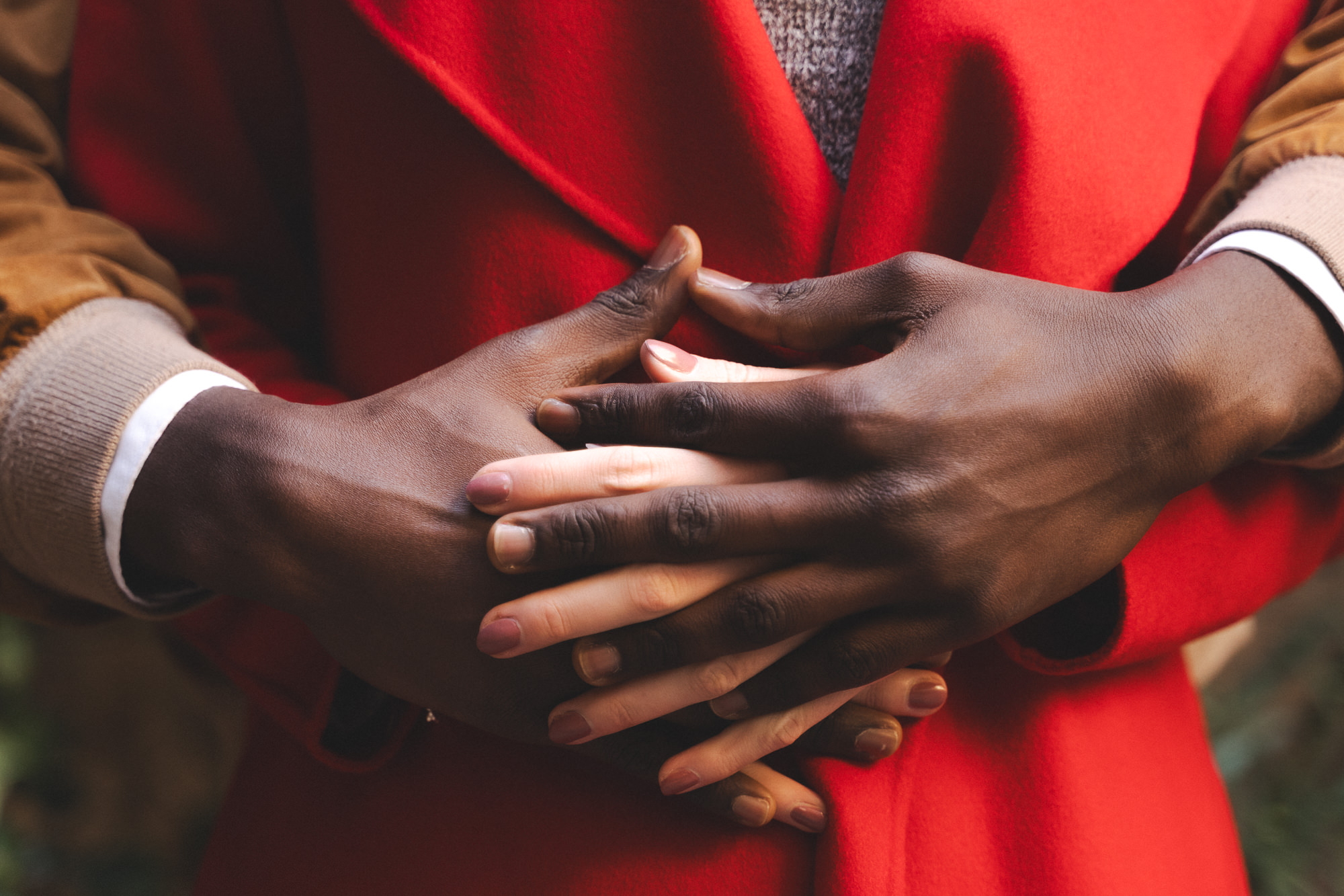 Close-up of intertwined hands resting on a red wool coat.