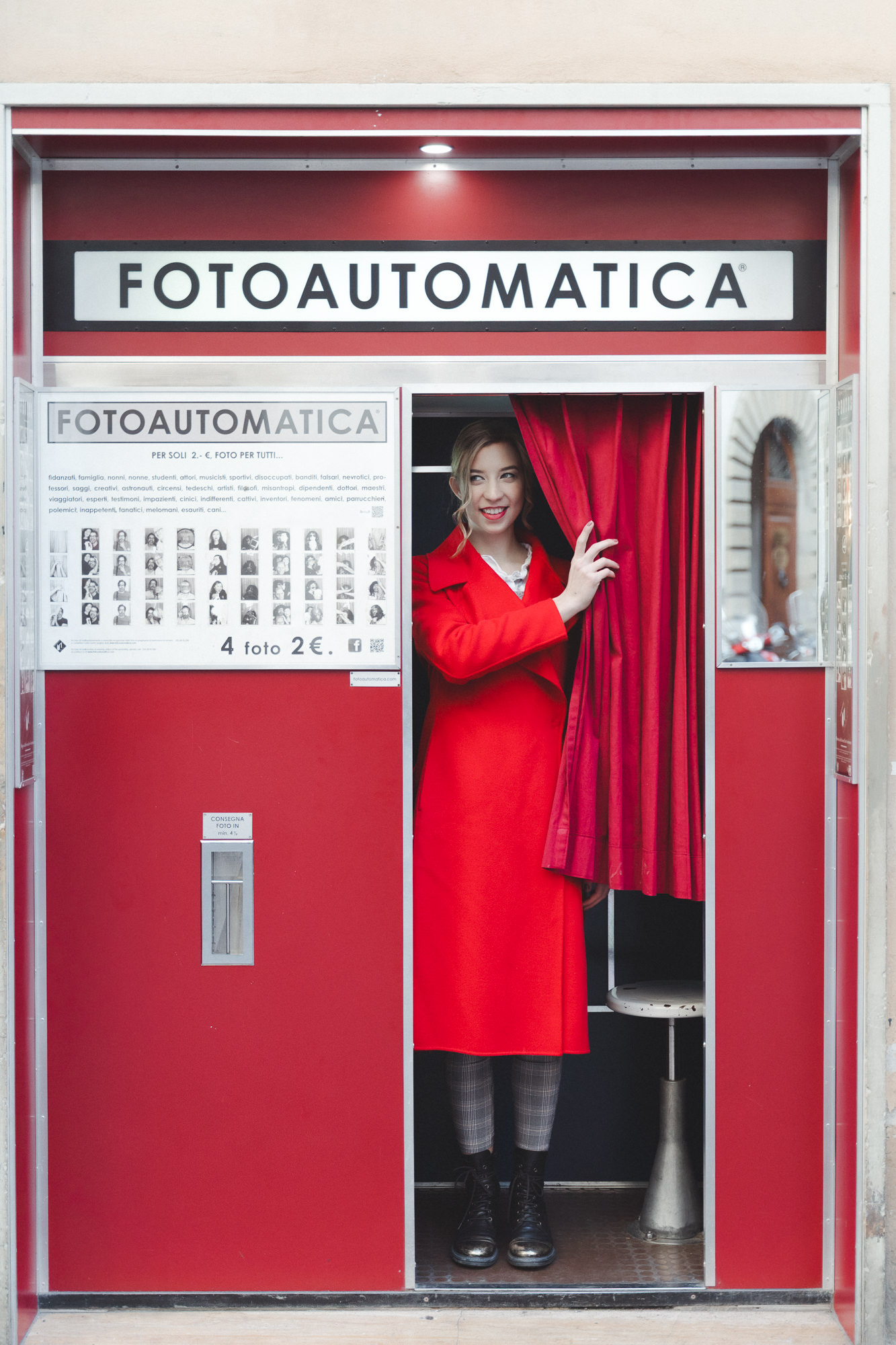 Woman in a red coat entering the red "Fotoautomatica" booth in Florence.