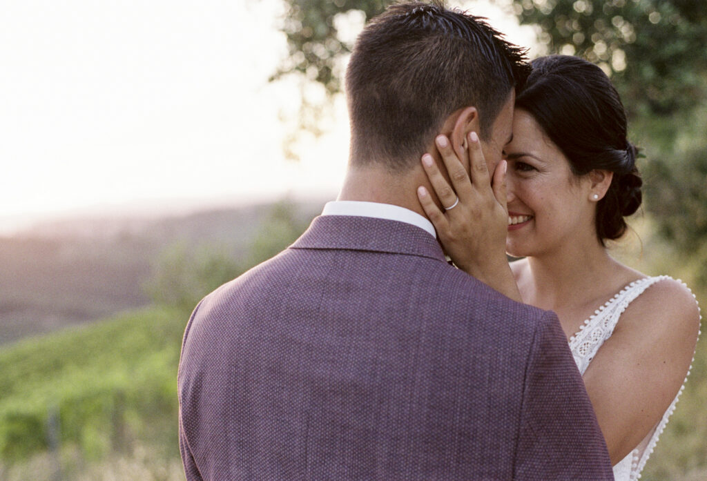 Bride smiling as she gently holds her partner’s face during a wedding portrait, photographed on film